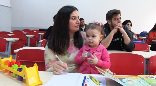 Kucağında çocuğu elinde kalemi ile okul sıralarında